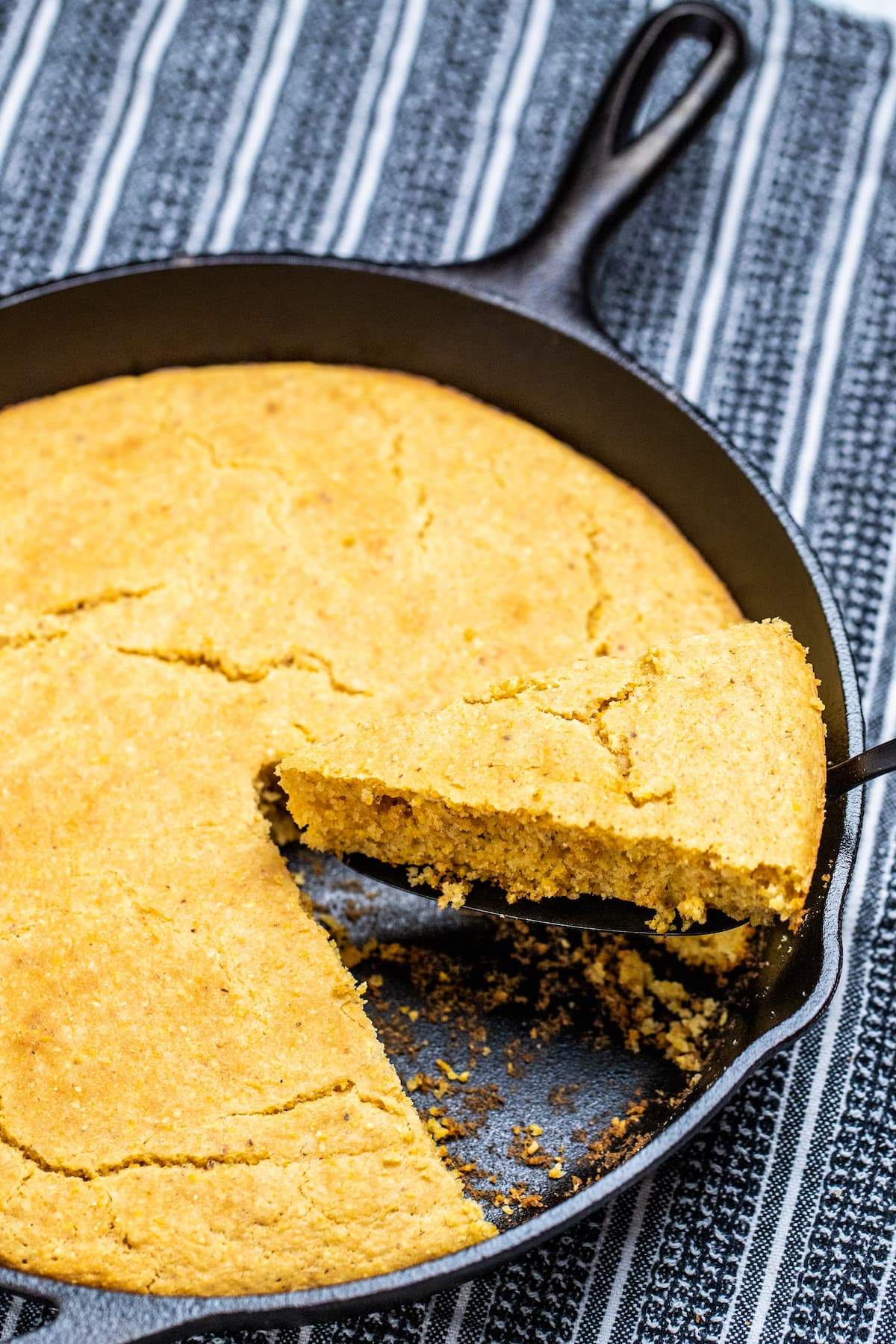 A cast iron skillet of gluten free cornbread with a slice being lifted out.