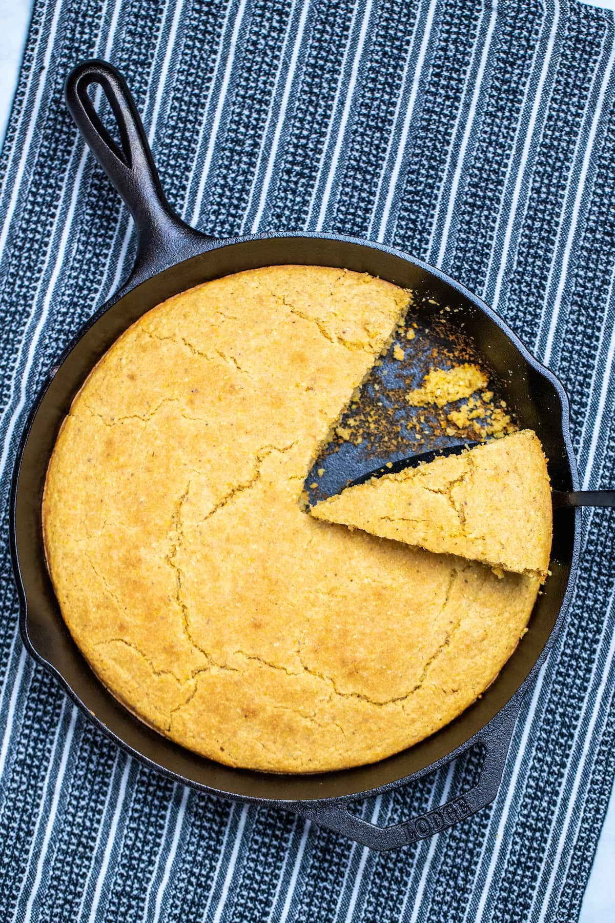 A cast iron skillet of gluten free cornbread with a slice being lifted out.