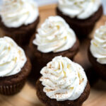 Cupcakes on a wooden cutting board with whipped cream cheese frosting decoratively piped on top and sprinkled with cinnamon.