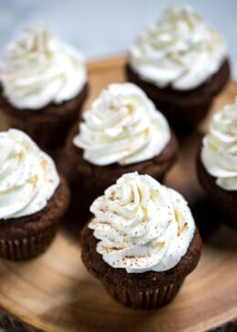 Cupcakes on a wooden cutting board with whipped cream cheese frosting decoratively piped on top and sprinkled with cinnamon.