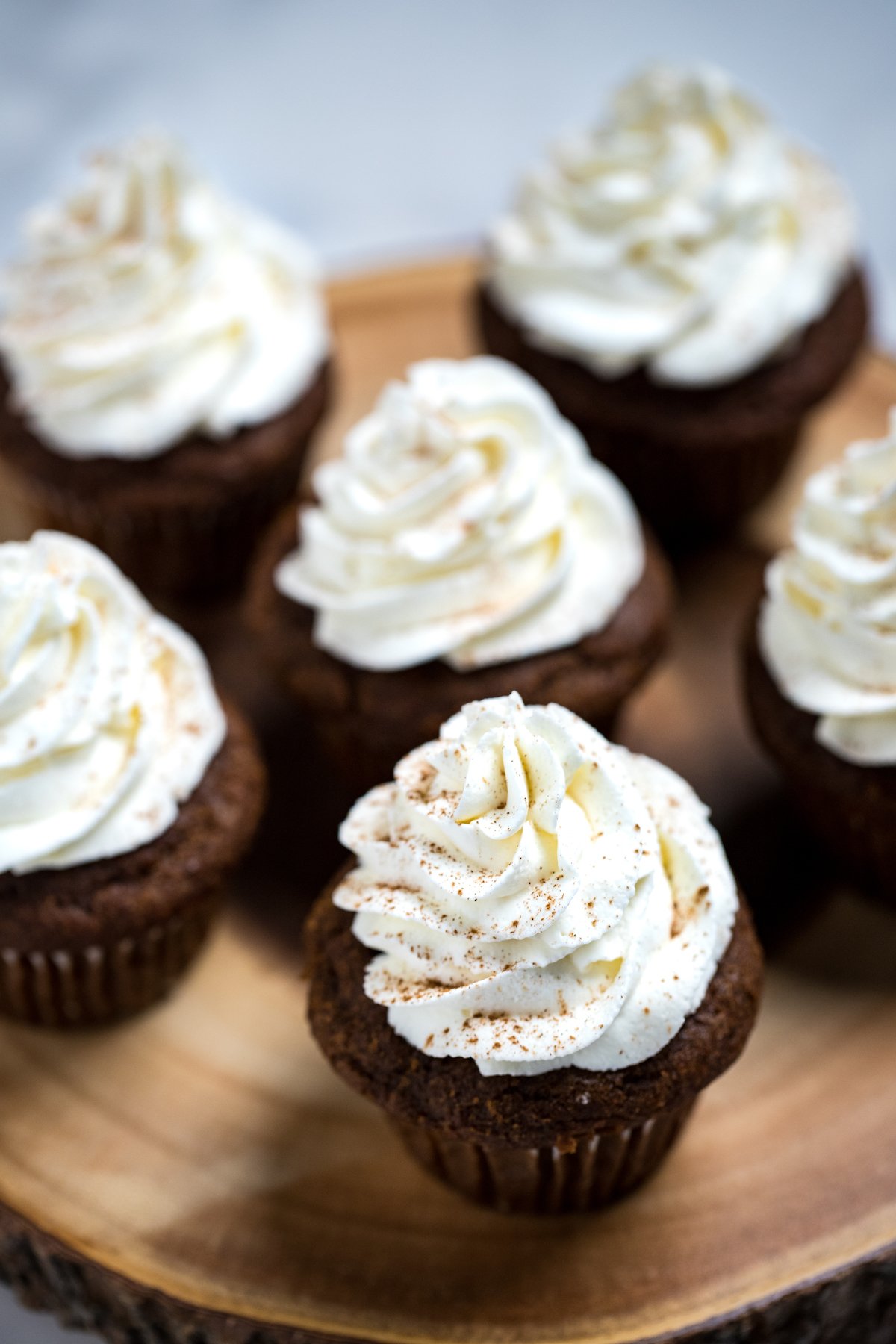 Cupcakes on a wooden cutting board with whipped cream cheese frosting decoratively piped on top and sprinkled with cinnamon.