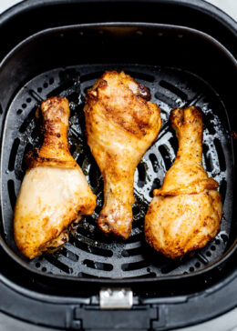 Three fully cooked chicken drumsticks in an air fryer basket.