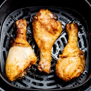 Three fully cooked chicken drumsticks in an air fryer basket.