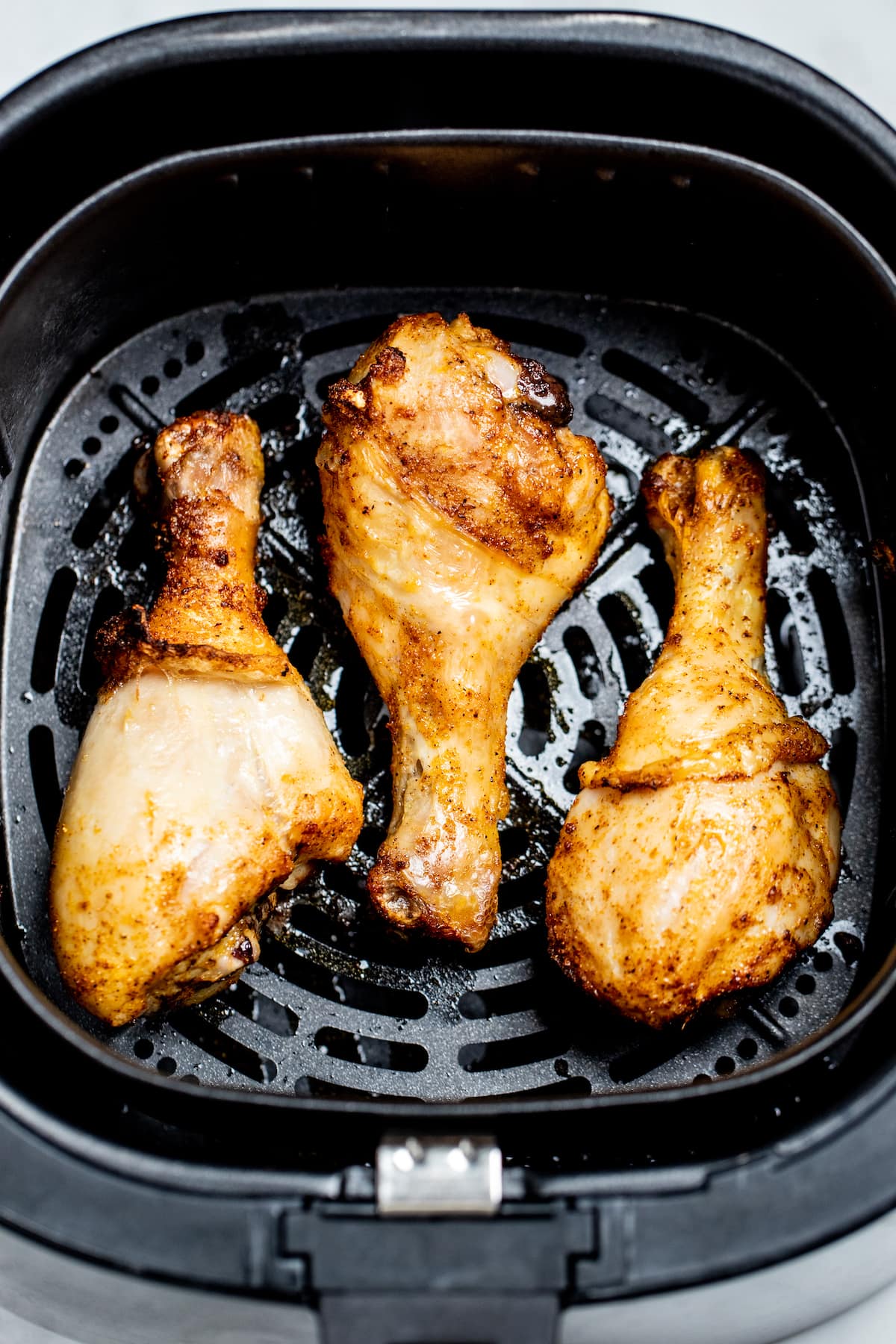 Three fully cooked chicken drumsticks in an air fryer basket.