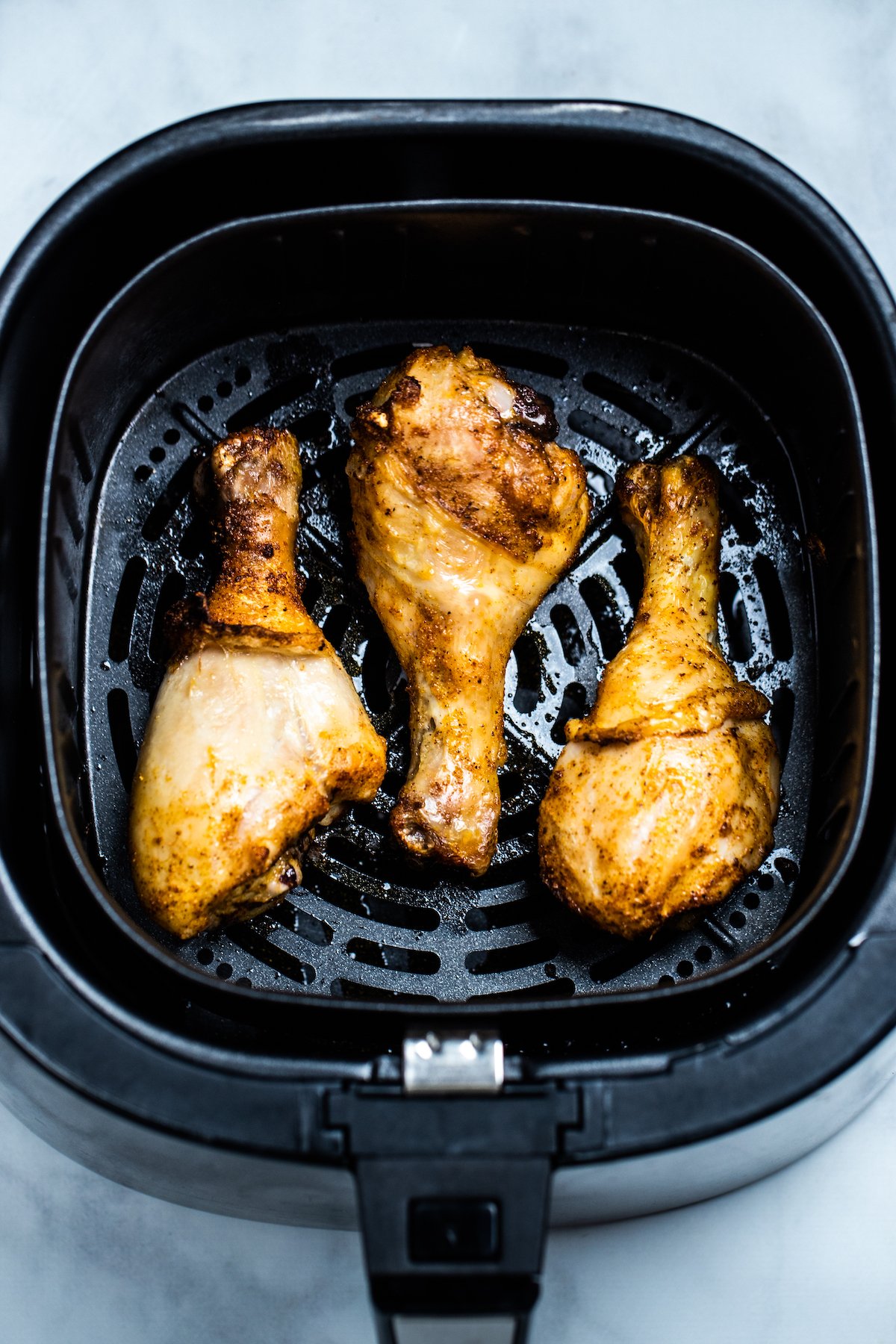 Three fully cooked chicken drumsticks in an air fryer basket.