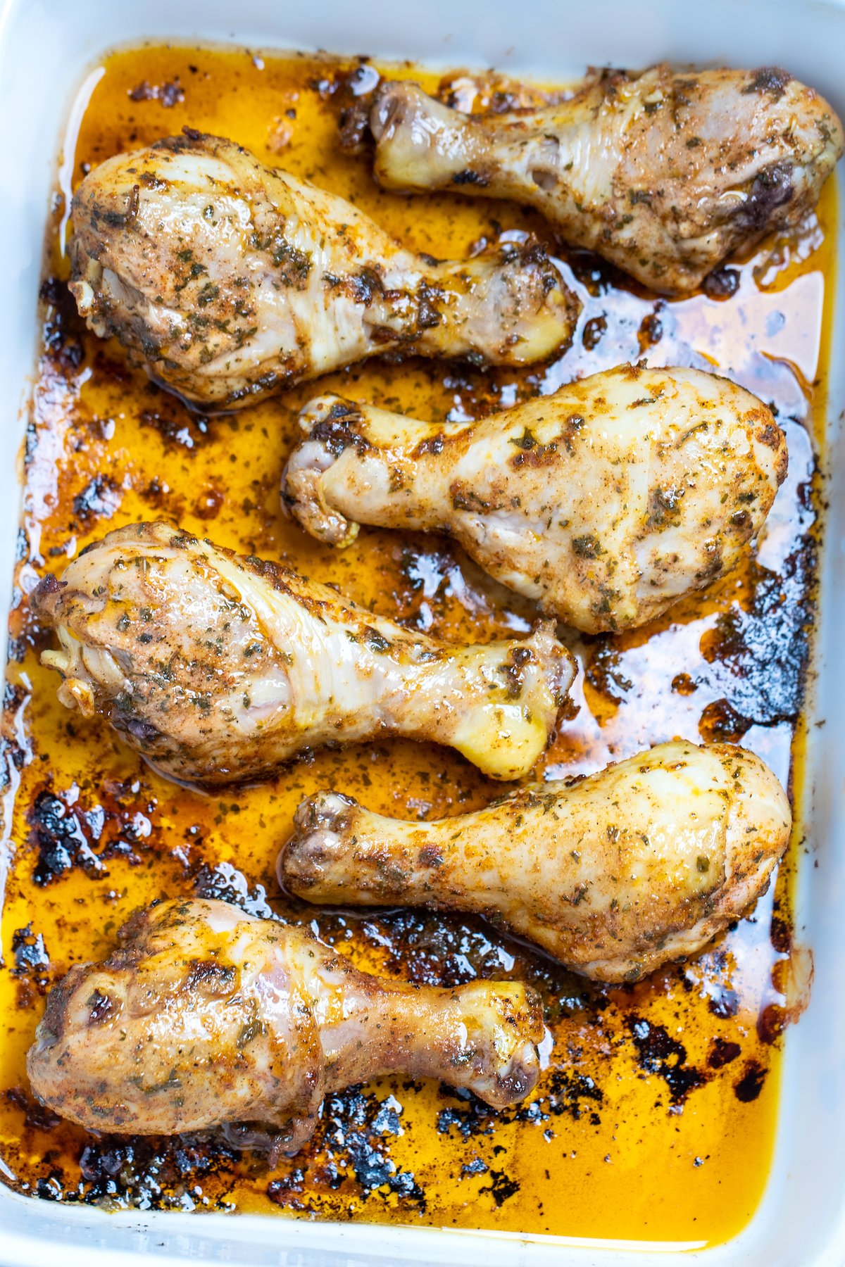 A baking dish with cooked chicken drumsticks covered in marinade.