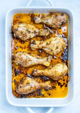 A baking dish with cooked chicken drumsticks covered in marinade.