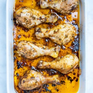 A baking dish with cooked chicken drumsticks covered in marinade.