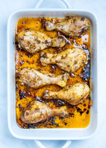 A baking dish with cooked chicken drumsticks covered in marinade.