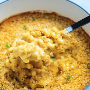 A dutch oven of gluten free mac and cheese topped with breadcrumbs with a spoon scooping some out.