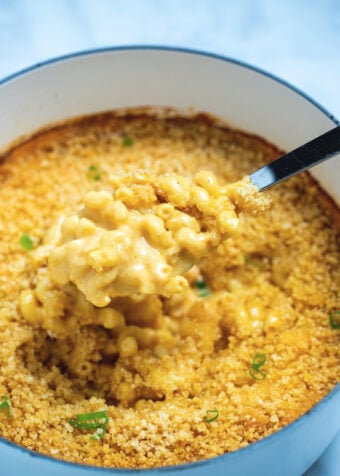 A dutch oven of gluten free mac and cheese topped with breadcrumbs with a spoon scooping some out.