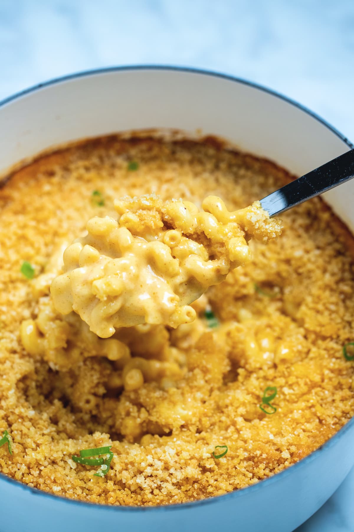 A dutch oven of gluten free mac and cheese topped with breadcrumbs with a spoon scooping some out.