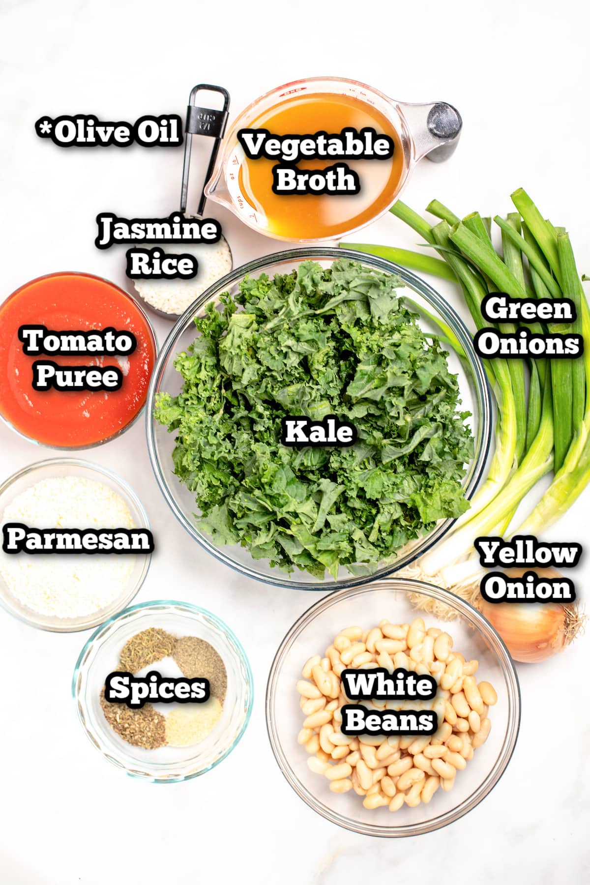 Individual ingredients for kale and white bean soup on a marble table.