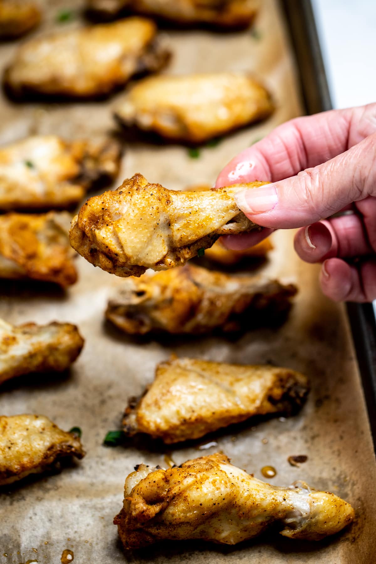 Instant pot chicken wings on a sheet pan lined with parchment paper topped with green onion, and a hand holding a wing.