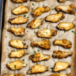 Instant pot chicken wings on a sheet pan lined with parchment paper topped with green onions.