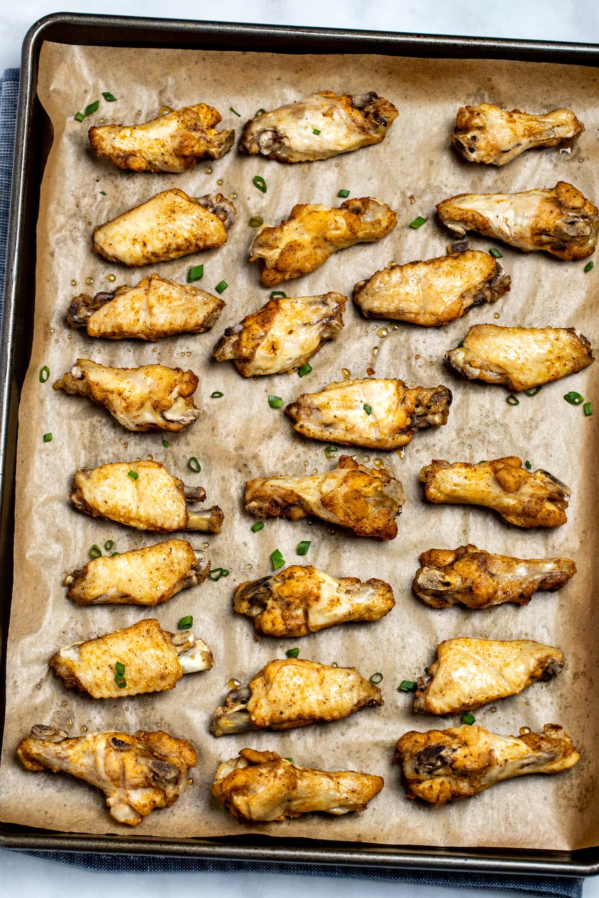 Instant pot chicken wings on a sheet pan lined with parchment paper topped with green onions.