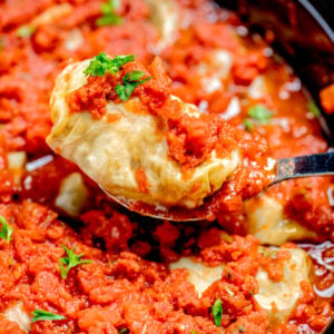 A spoon lifting a stuffed cabbage roll out of the slow cooker, topped with tomato sauce and fresh parsley.