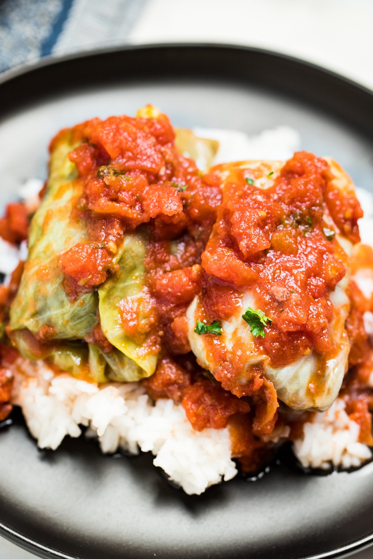 Two crockpot cabbage rolls topped with tomato sauce on top of a bed of rice on a plate.