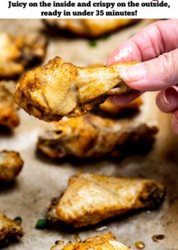 Pinterest pin with instant pot chicken wings on a sheet pan lined with parchment paper topped with green onions, and a hand holding a wing.