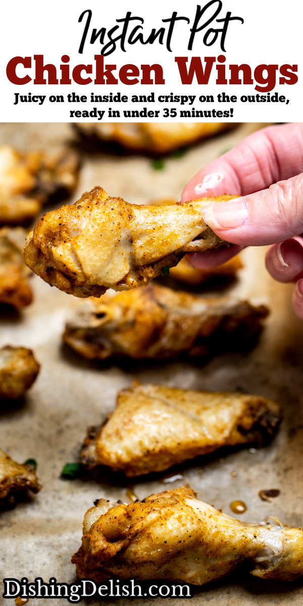 Pinterest pin with instant pot chicken wings on a sheet pan lined with parchment paper topped with green onions, and a hand holding a wing.