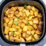 Breakfast potatoes fully cooked in an air fryer basket on a table.