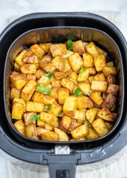 Breakfast potatoes fully cooked in an air fryer basket on a table.