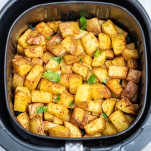 Breakfast potatoes fully cooked in an air fryer basket on a table.
