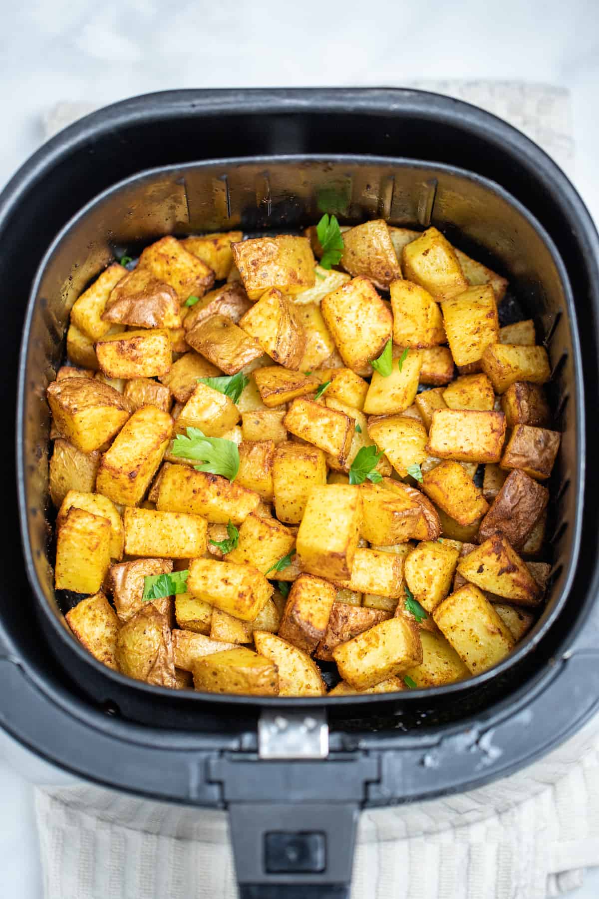 Breakfast potatoes fully cooked in an air fryer basket on a table.