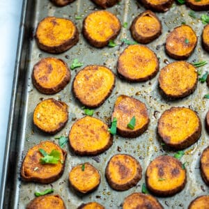 Sweet potato slices on a sheet pan with parchment paper, fully cooked with caramelized tops and fresh parsley on top.