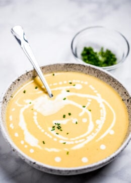 A bowl of cauliflower soup on a table, with cream drizzled on top and fresh chives.