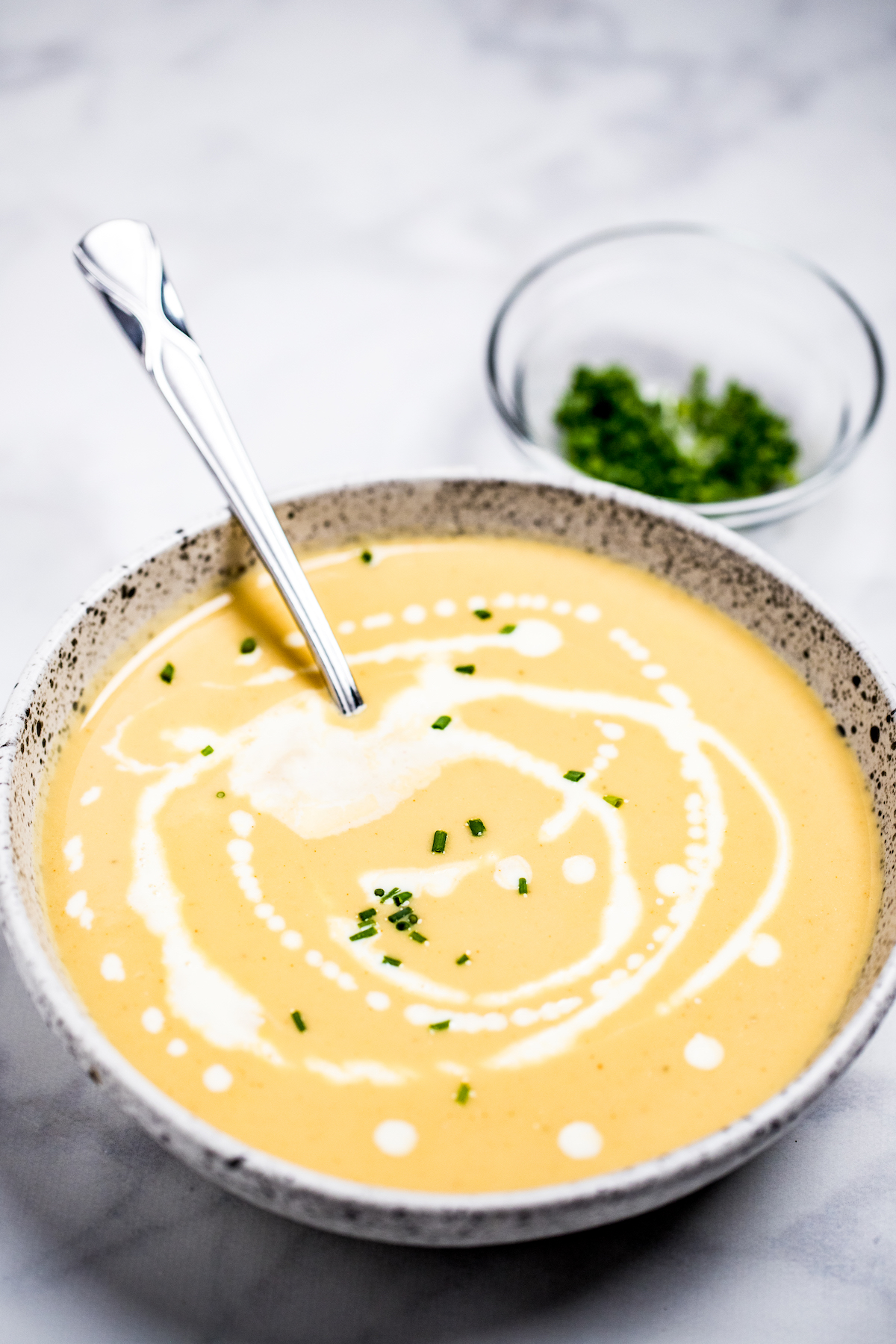 A bowl of cauliflower soup on a table, with cream drizzled on top and fresh chives.