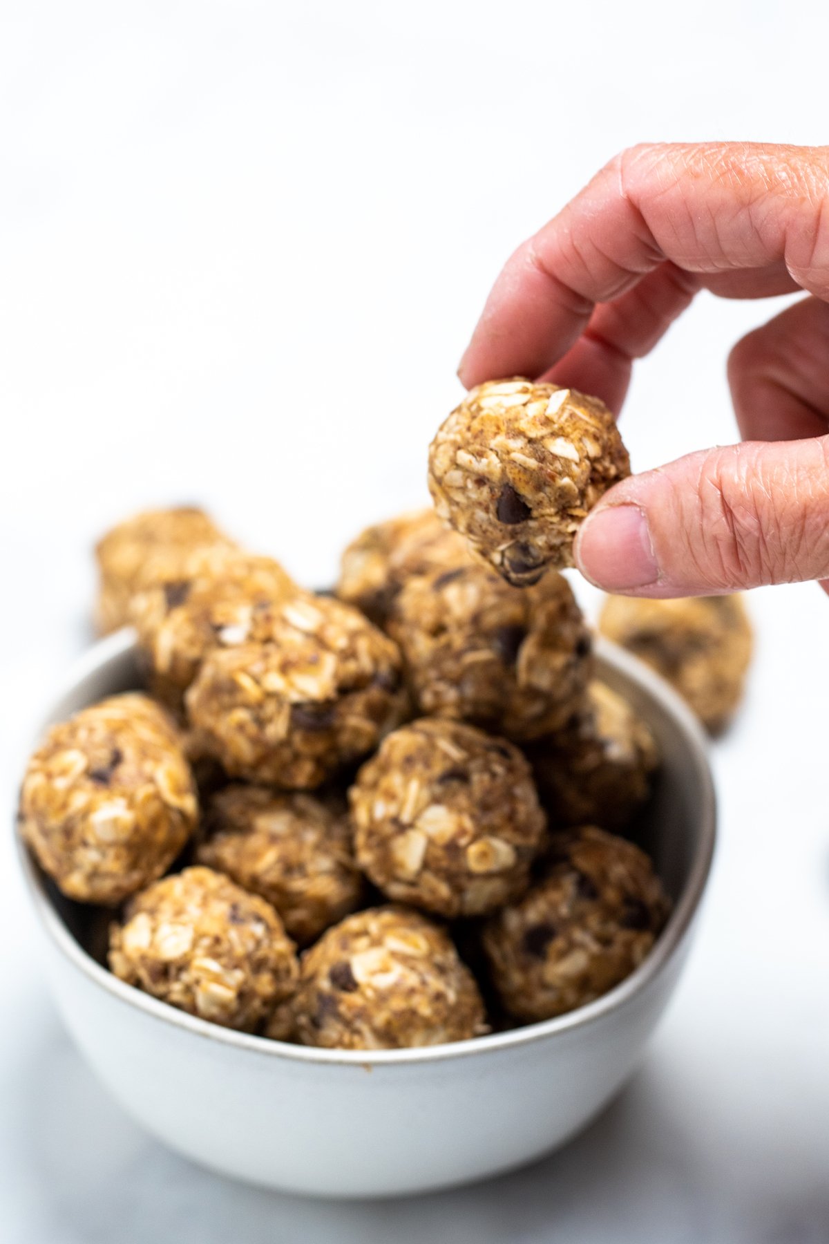 A hand taking a peanut butter oat ball from a bowl.