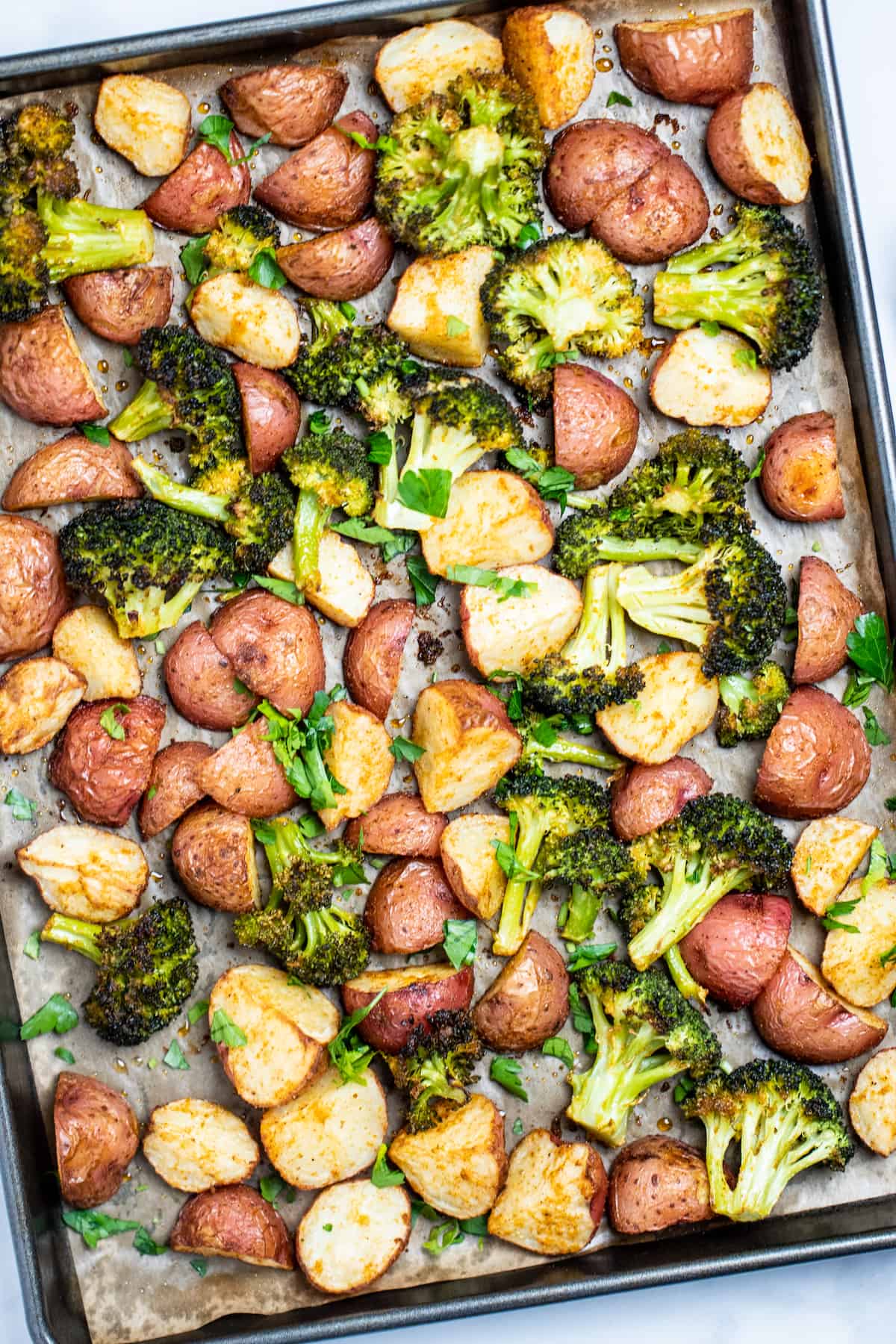 Roasted potatoes and broccoli on a sheet pan with parchment paper.