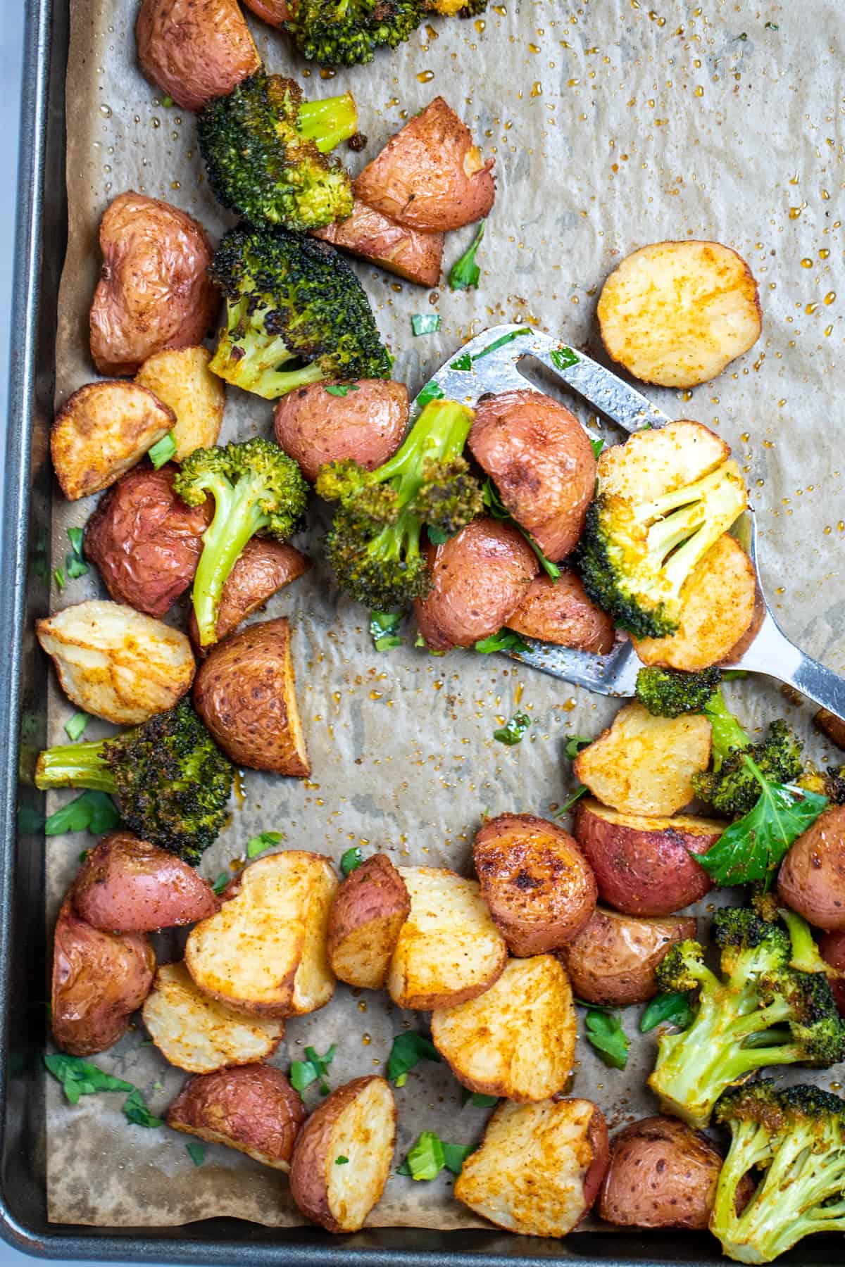 Roasted potatoes and broccoli on a sheet pan with parchment paper.