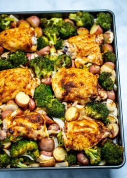 A sheet pan with broccoli, potatoes, sliced onions, and chicken thighs fully cooked and golden brown.