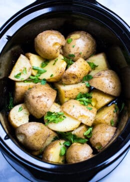 Quartered gold potatoes in a slow cooker topped with fresh parsley.
