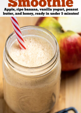 Pinterest pin with an apple smoothie in a mason jar with a straw sitting on a wooden cutting board with a teaspoon of cinnamon in front of it, and an apple cut in half behind it.