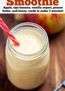 Pinterest pin with an apple banana smoothie in a mason jar with a straw on a wooden cutting board with an apple cut in half behind it and a teaspoon of cinnamon in front of it.