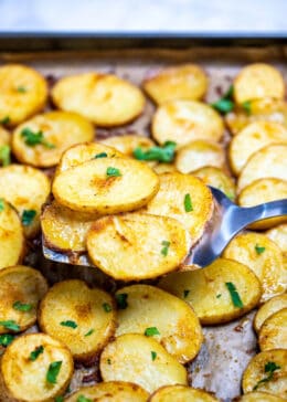 A spatula lifting baked potato slices up from a sheet pan.