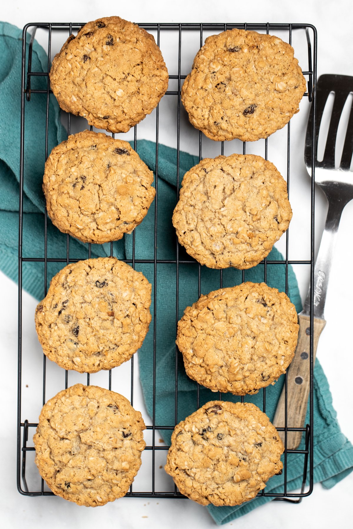 Gluten free oatmeal cookies on a cooling rack over a kitchen towel with a spatula on the side.