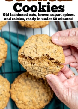 Pinterest pin with a hand breaking a cookie in half, over a cooling rack of other gluten free oatmeal cookies.