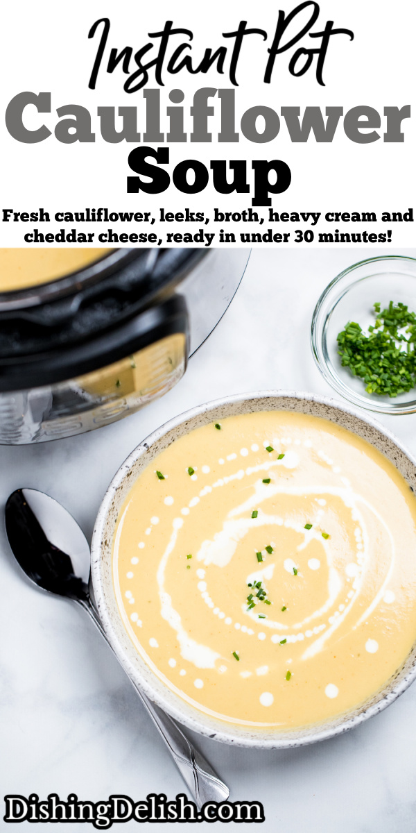 A bowl of cauliflower soup on a table in front of an instant pot, with cream drizzled on top and fresh chives next to a spoon.