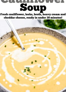 A bowl of cauliflower soup on a table, with cream drizzled on top and fresh chives.