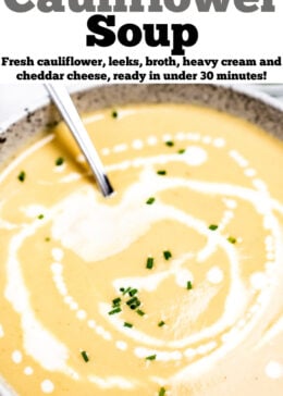 A bowl of cauliflower soup on a table, with cream drizzled on top and fresh chives.