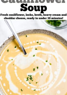 A bowl of cauliflower soup on a table, with cream drizzled on top and fresh chives.