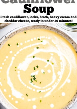 A bowl of cauliflower soup on a table, with cream drizzled on top and fresh chives.