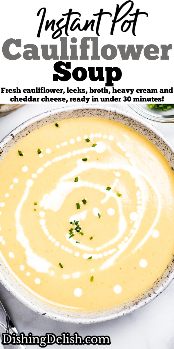 A bowl of cauliflower soup on a table, with cream drizzled on top and fresh chives.