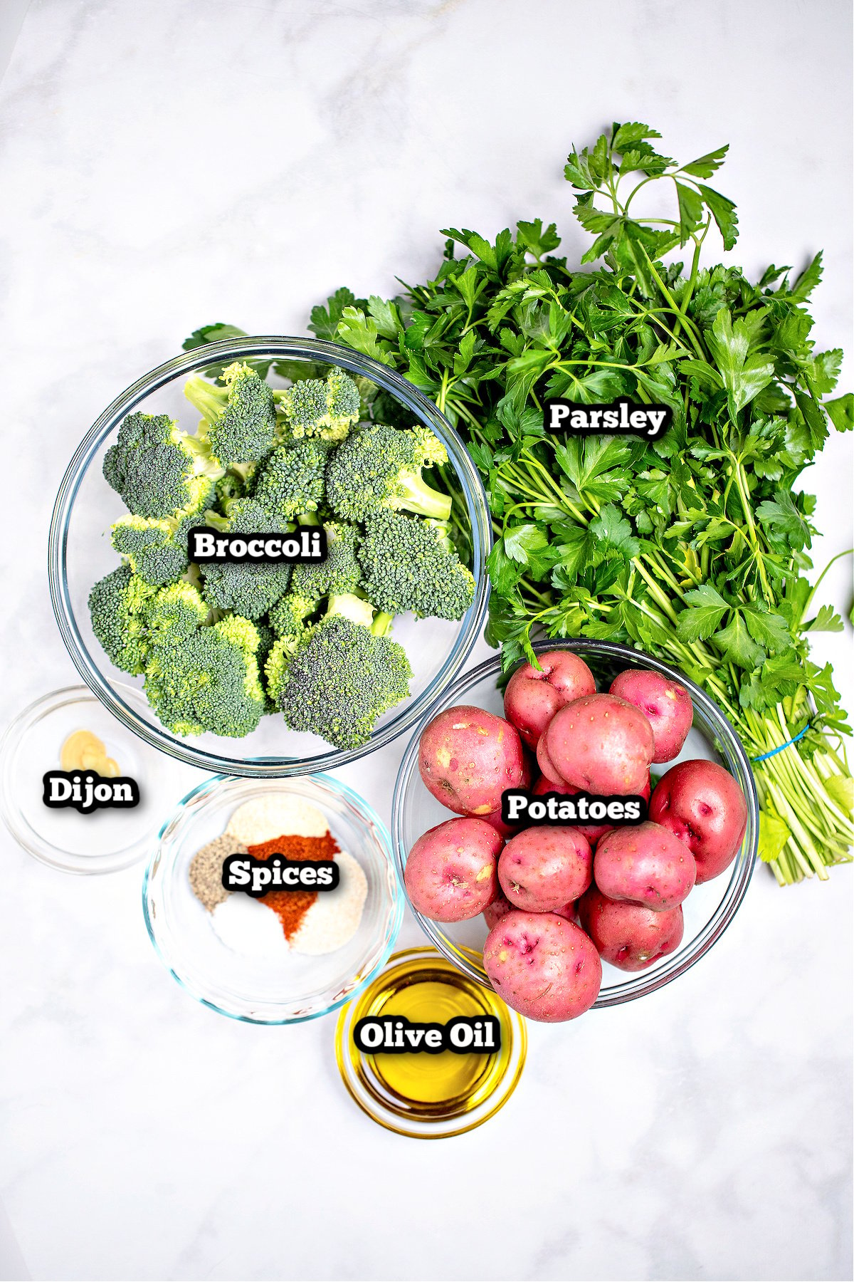 Individual ingredients for roasted potatoes and broccoli on a marble table.