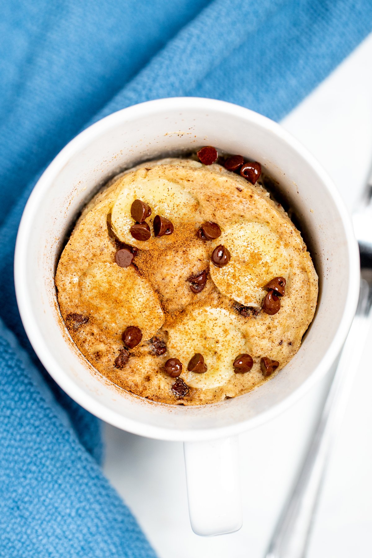 A coffee mug with a banana mug cake topped with banana slices, cinnamon, and mini chocolate chips.