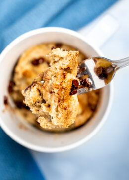 A fork lifting a piece of banana mug cake out of the mug with cinnamon and mini chocolate chips on top.